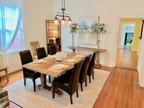 Une salle à manger avec une table en bois dressée pour six personnes, entourée de chaises noires. Un lustre est suspendu au-dessus de la table, un miroir orne le mur, et un tableau est accroché.