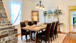 A dining area with a wooden table set for six, surrounded by dark chairs, a hanging light fixture, and a painting on the wall. - The RED DOOR: Explore Pensacola's Downtown Entertainment next to Wedding Venues! (Pensacola)