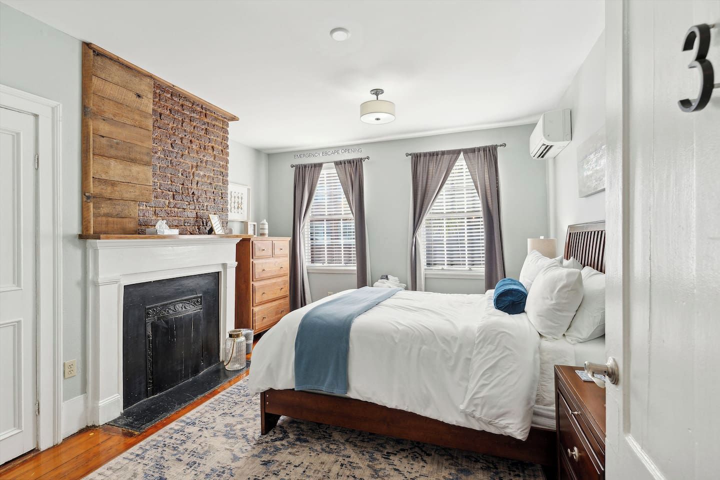 A bedroom with a fireplace, a bed with white bedding, a wooden headboard, and a number '3' on the wall.