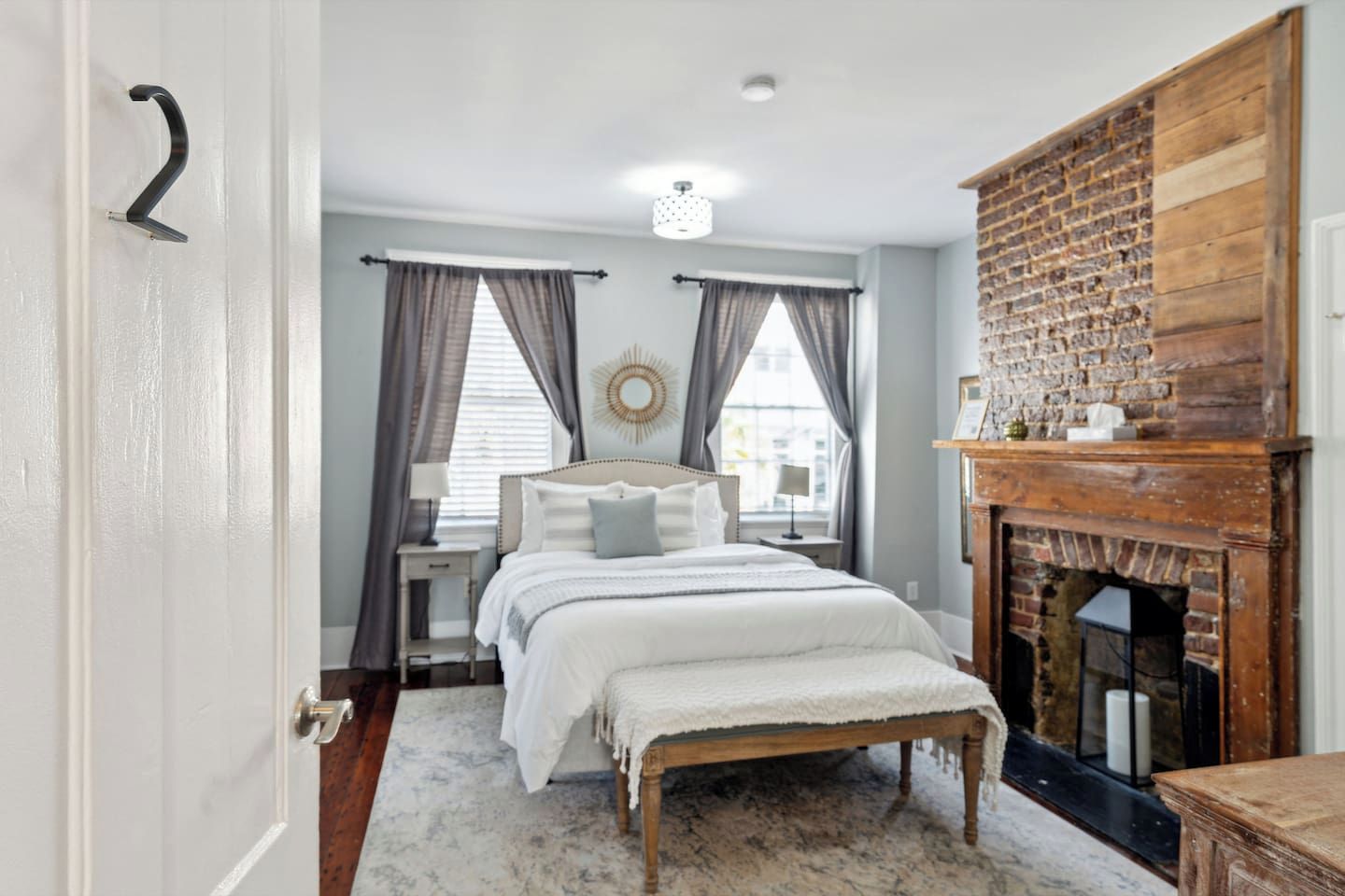 A bedroom with a bed, a nightstand, a dresser, a fireplace, and a door with a number.