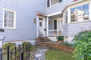 Una casa de dos pisos con un porche delantero, un acceso de ladrillo y un sendero de piedra que lleva a la puerta.