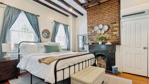 A bedroom with a bed, a bench, a fireplace, and a door. - Downtown home 5BR & 7 Beds w/ Free Private Parking (Charleston)