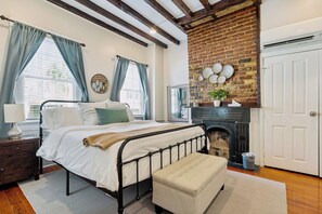 A bedroom with a bed, a bench, a fireplace, and a door. - Downtown home 5BR & 7 Beds w/ Free Private Parking (Charleston)