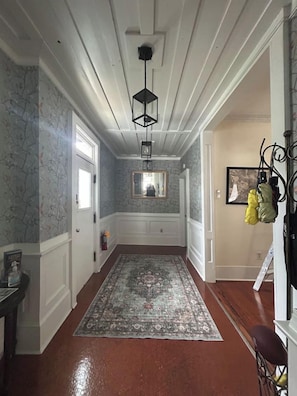 Un pasillo con un tapete estampado, una lámpara colgante y una puerta que da a otra habitación.