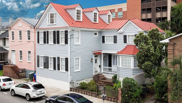 A two-story residential building with a red roof, white siding, and a front porch. - Downtown home 5BR & 7 Beds w/ Free Private Parking (Charleston)
