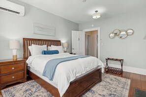 Un dormitorio con cama de madera, mesitas de noche, un armario y aire acondicionado mural, una puerta y un espejo.
