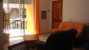 A living room with a black sofa, a wooden table, and a balcony with orange curtains.