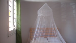 A single bed with a canopy, a window with blinds, and a green curtain.