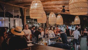 Un bar ple d'ambient, amb llums penjants de vímet, sostre de fusta i zona de bar amb ampolles i vasos.