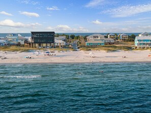 A beachfront property with a sandy beach, ocean view, and several buildings with large windows and balconies.