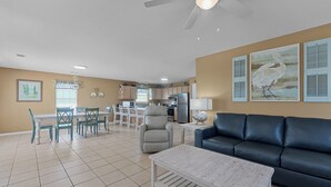 A living room with a black sofa, a white coffee table, and a dining area with a white table and chairs. - Spacious house within walking distance from beach- less then 100 yards (Gulf Shores)