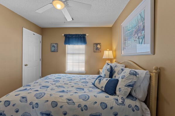 A bedroom with a bed, a ceiling fan, a window with blinds, and wall art.
