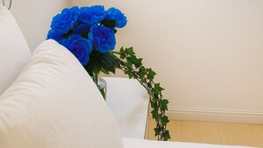Una stanza con vista sull'oceano attraverso una finestra, un divano bianco e un vaso con fiori blu.