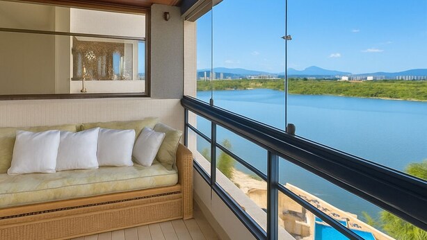 Un balcone con un divano in vimini, vista su un lago e cielo sereno.