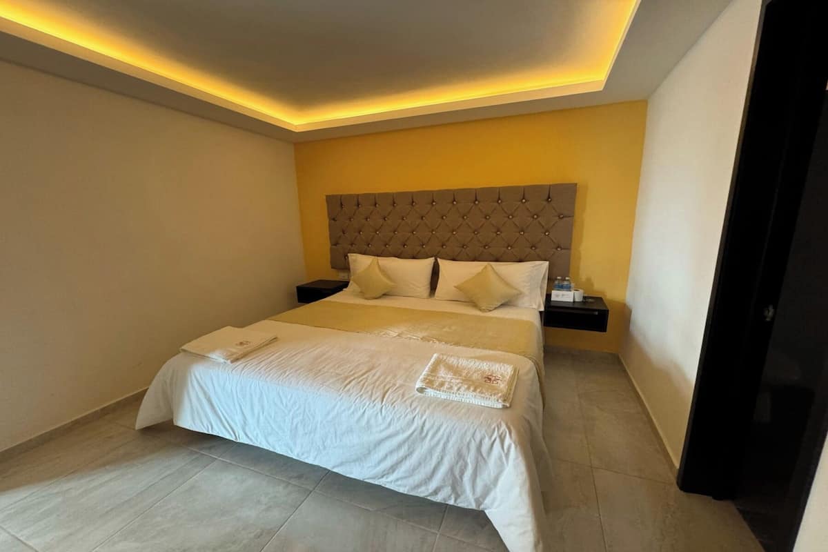 Una habitación de hotel con una cama grande, un cabecero capitonado y una mesita de noche con lámpara.