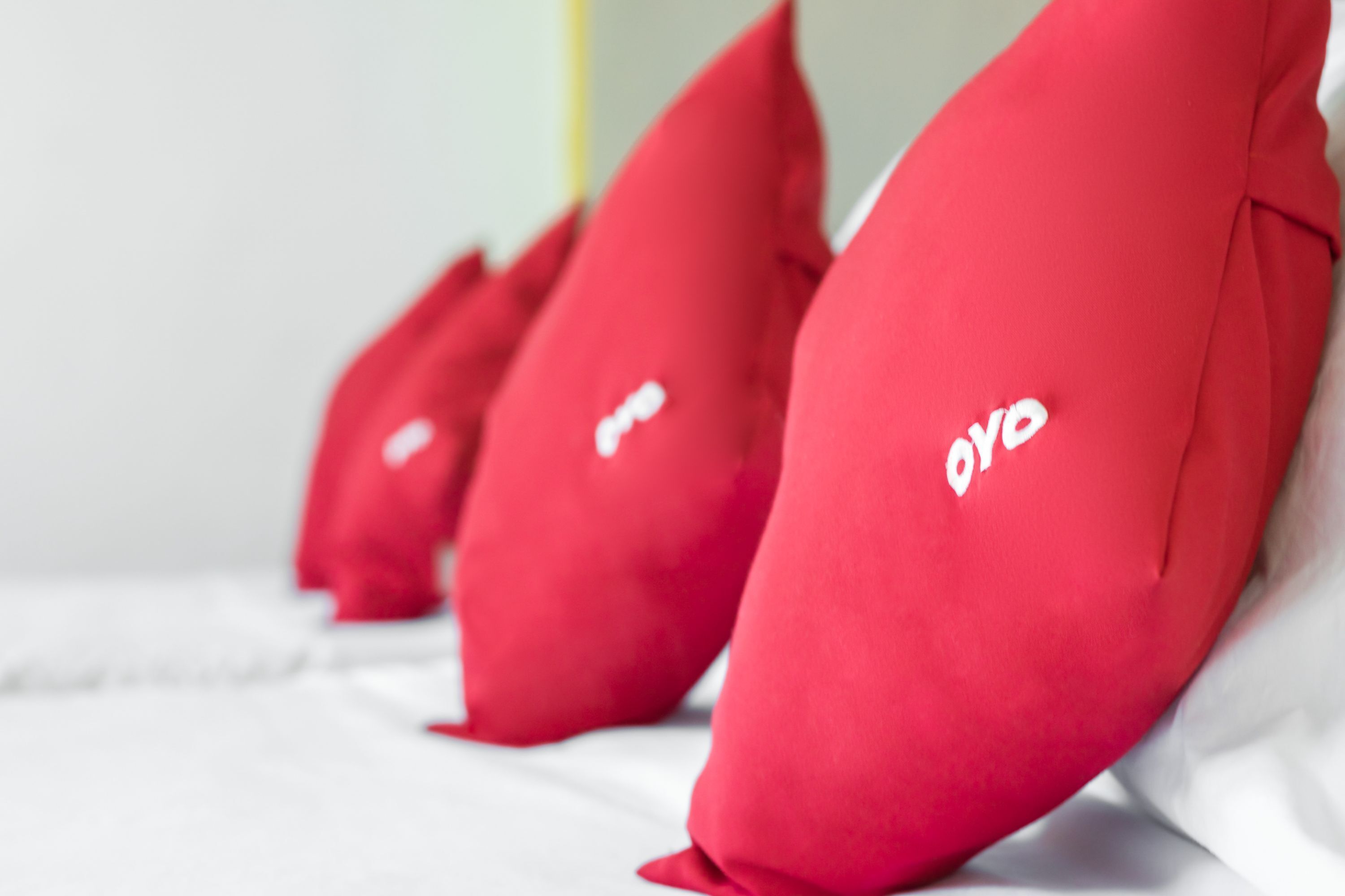 A row of red pillows with a white logo on a bed.