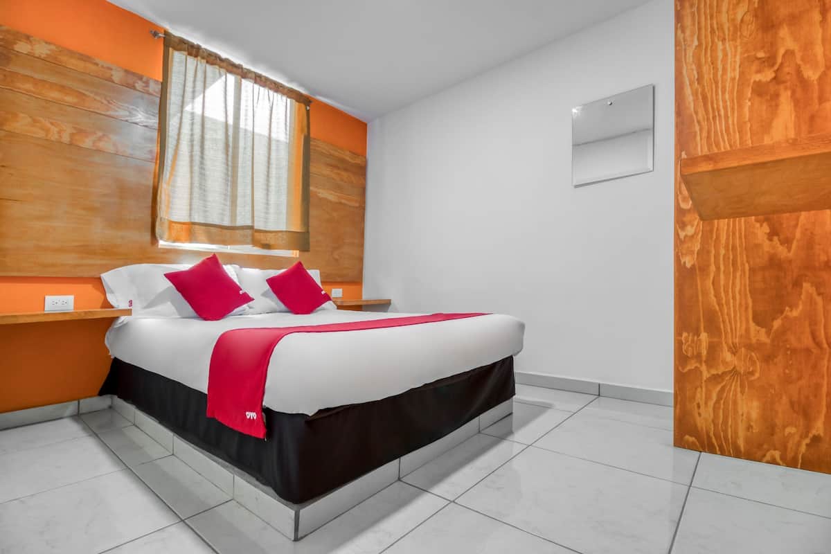 Una habitación de hotel moderna con una cama grande, cabecera de madera y una ventana con cortinas.