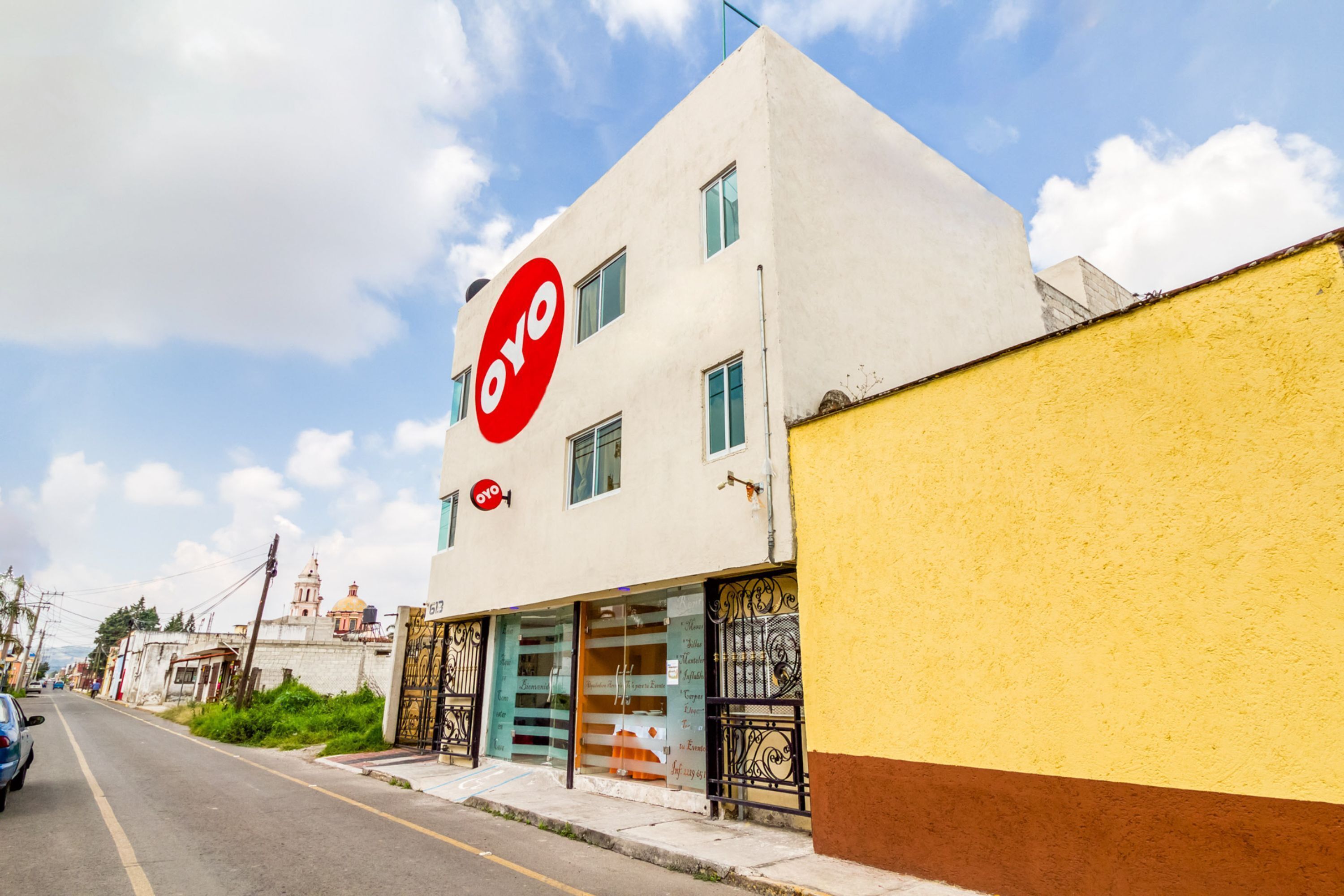 Un edificio con un letrero grande rojo y blanco, una pared amarilla y una calle al fondo.