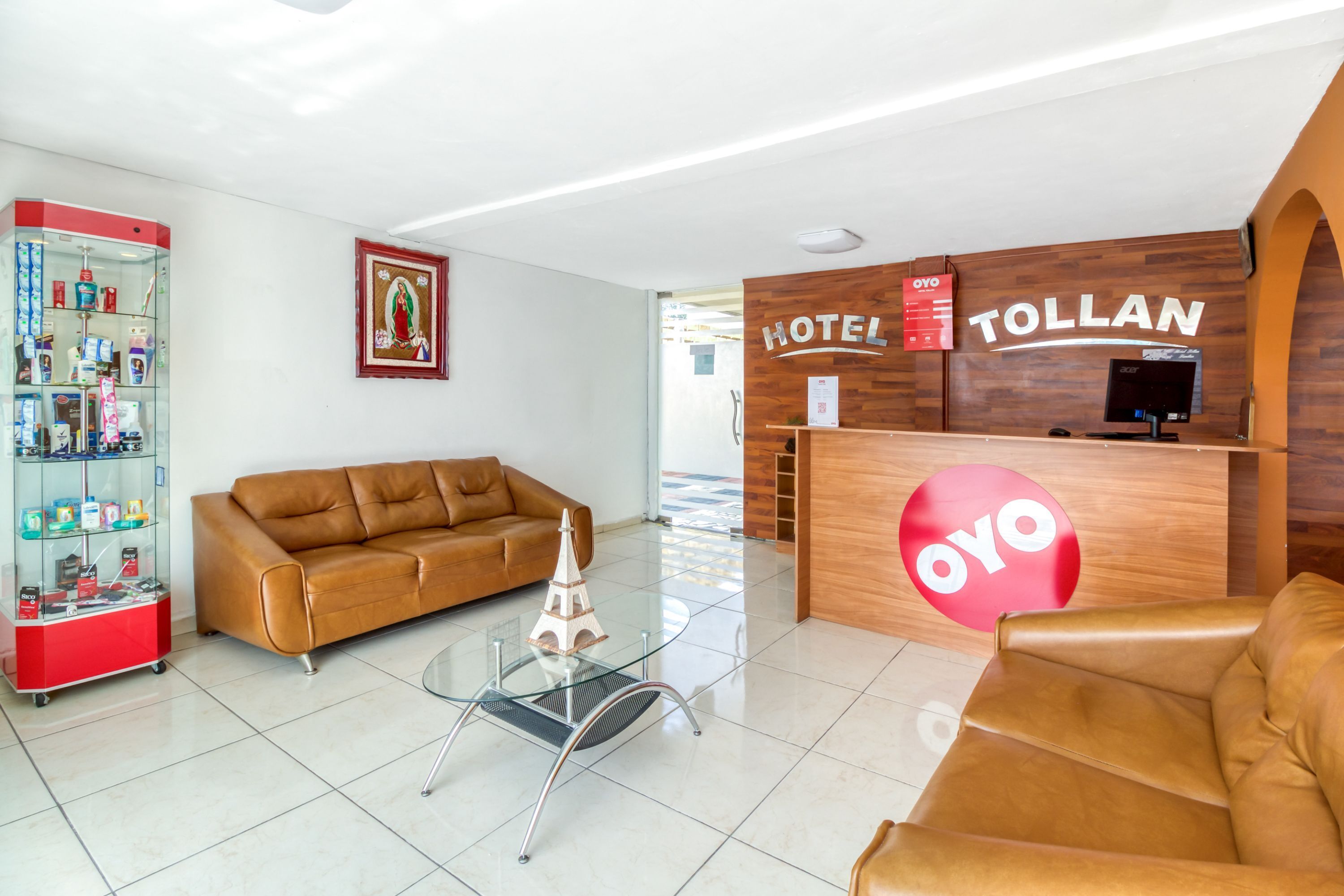 A hotel lobby with a reception desk, a brown leather sofa, a glass coffee table with a model, and a vending machine.