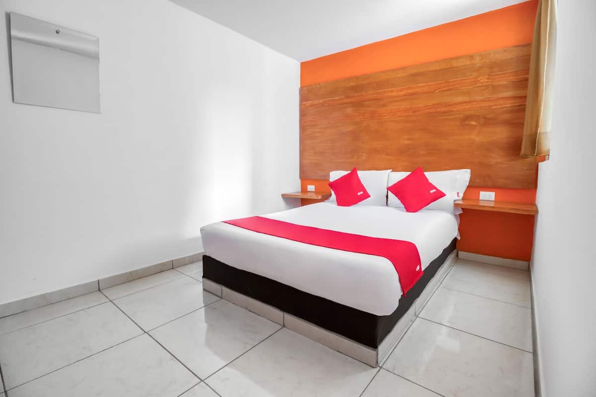 Una habitación de hotel moderna con una cama grande, paredes blancas y una pared de acento naranja.