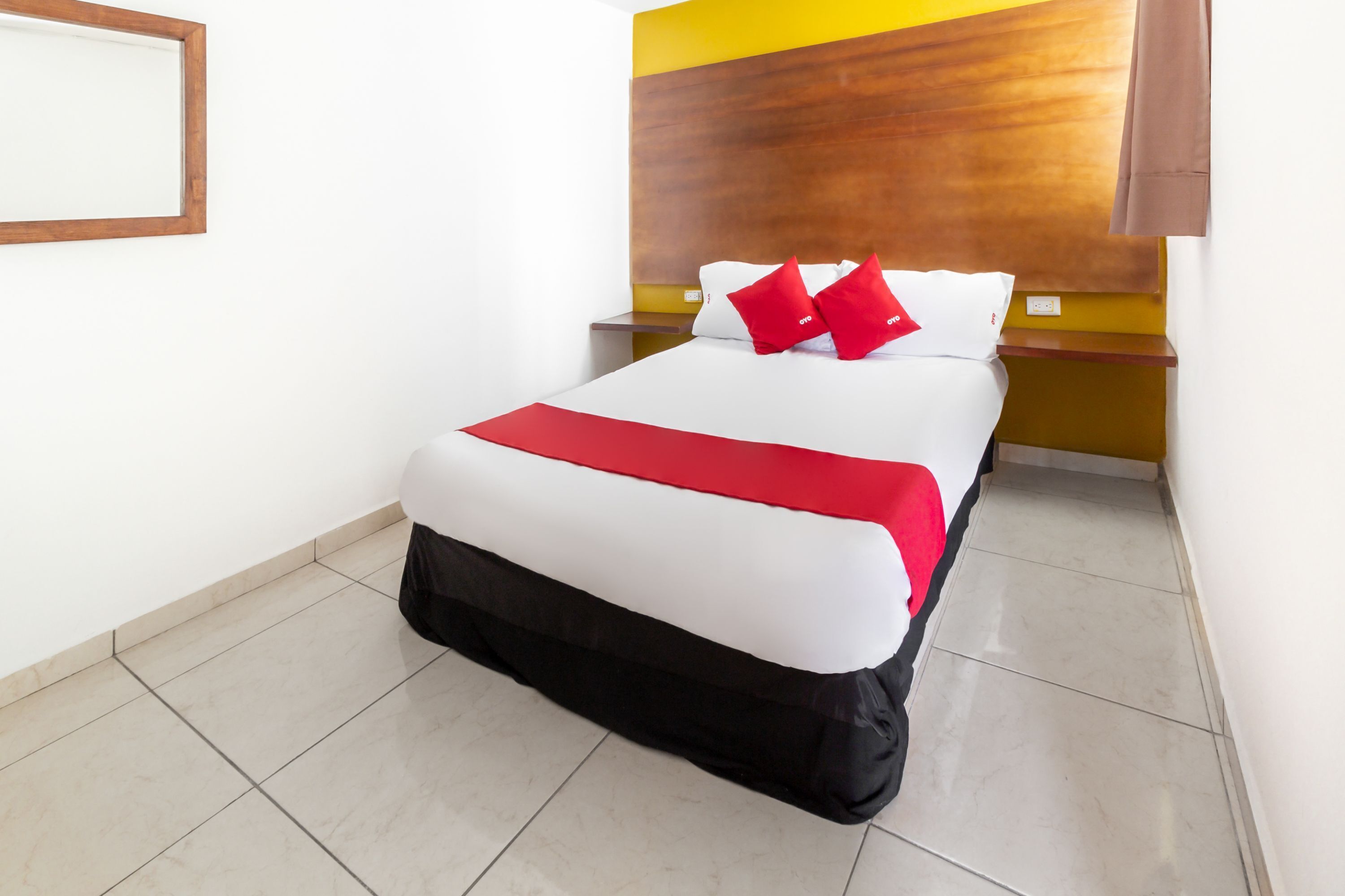 A neatly made bed with a white and red bedspread, a black skirt, and two red pillows.