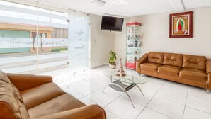 A modern living room with a brown leather sofa, a glass coffee table, and a television mounted on the wall. - OYO Hotel Familiar Tollan Cholula (San Pedro Cholula)