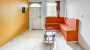 A room with a yellow wall, a white door, an orange sofa, and a glass table. - OYO Hotel Familiar Tollan Cholula (San Pedro Cholula)