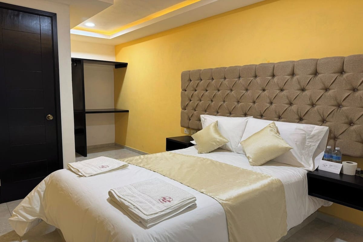 Una habitación de hotel con una cama grande, cabecera, mesita de noche y una puerta.