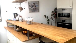 Une cuisine avec un plan de travail en bois, un luminaire suspendu, une cuisinière et un tableau accroché au mur.