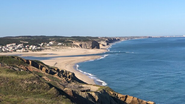 Un paysage côtier avec une plage, des falaises rocheuses et une ville située au loin.