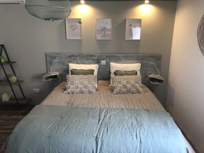 Een slaapkamer met een bed, twee nachtkastjes, een wandplank en drie ingelijste kunstwerken.