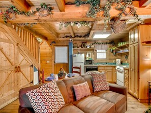 A cozy cabin interior with a wooden dining table, a sofa with patterned cushions, and a kitchen area with wooden cabinets and appliances. - Precious Moments is the ultimate private retreat for that special occasion (Sevierville)