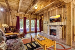 A log cabin interior with a fireplace, leather furniture, and a large window.