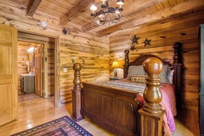 A wooden-paneled bedroom with a bed, a nightstand, a lamp, and a chandelier.