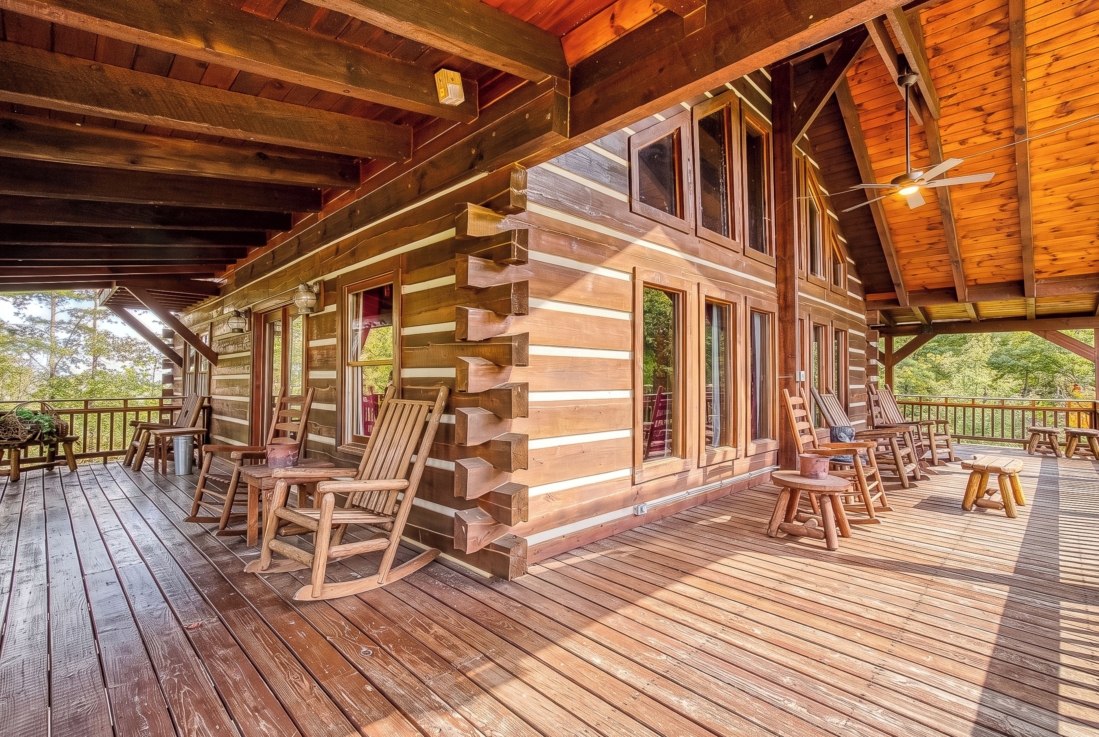 A log cabin with a deck furnished with chairs and tables, large windows, and a wooden ceiling.