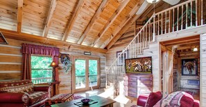A cabin interior with a wooden ceiling, a staircase, a sofa, a coffee table, and a television.