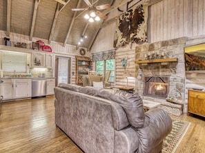 A log cabin interior with a stone fireplace, wooden ceiling, and a leather sofa.
