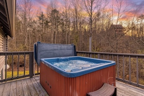 Un bain à remous sur une terrasse en bois, avec vue sur les arbres et un coucher de soleil.