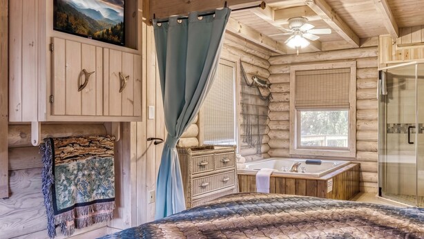 A log cabin bedroom with a bed, a mounted TV, a bathroom with a bathtub, and a shower.