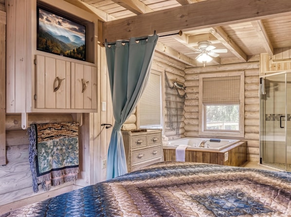 A log cabin interior with a bed, a bathroom, and a mounted television.