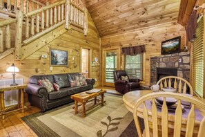 Un intérieur en bois avec un escalier, une cheminée, un canapé, un fauteuil et une table.
