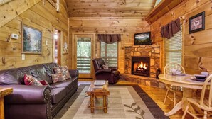 Un intérieur de chalet chaleureux avec un canapé en cuir, une cheminée en pierre et un coin repas.
