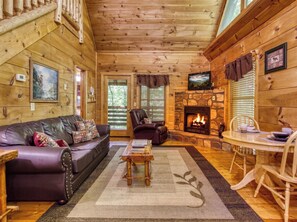 A cozy cabin interior with a leather sofa, a stone fireplace, and a dining area.