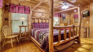 L’intérieur d’une cabane en bois, avec un lit, une chaise, une lampe et un ventilateur de plafond.