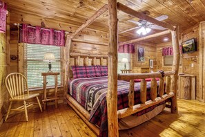 A wooden cabin interior with a bed, a chair, a lamp, and a ceiling fan.