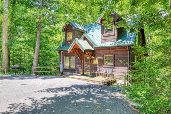 A rustic cabin with a porch, a mailbox, and a signboard.
