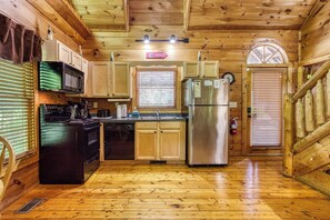 A wooden cabin interior with a kitchen featuring a microwave, stove, dishwasher, and refrigerator.