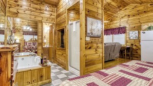 A wooden cabin interior with a large bed, a bathroom with a bathtub, a dining area, and a kitchen.