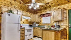 A wooden cabin kitchen with a refrigerator, stove, microwave, and wooden cabinets.
