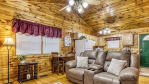 A cozy cabin interior with a leather sofa, wooden walls, a dining area, and a green door.